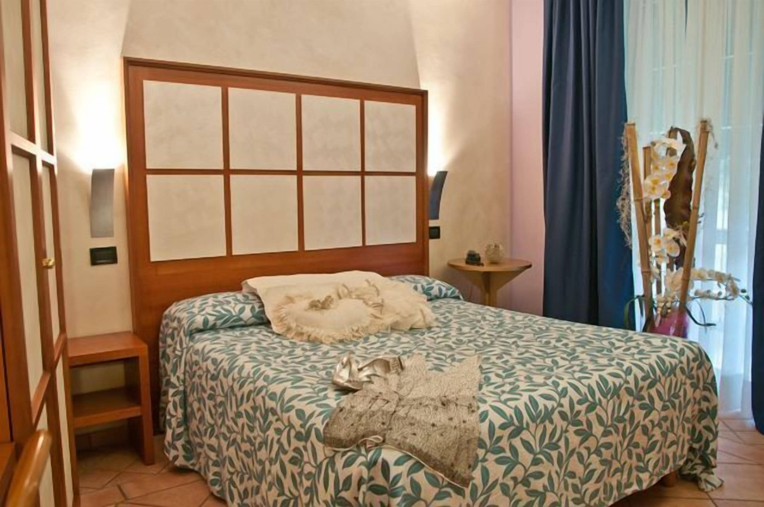 A bedroom with a large bed, a wooden headboard, a small bedside table, and a decorative plant.