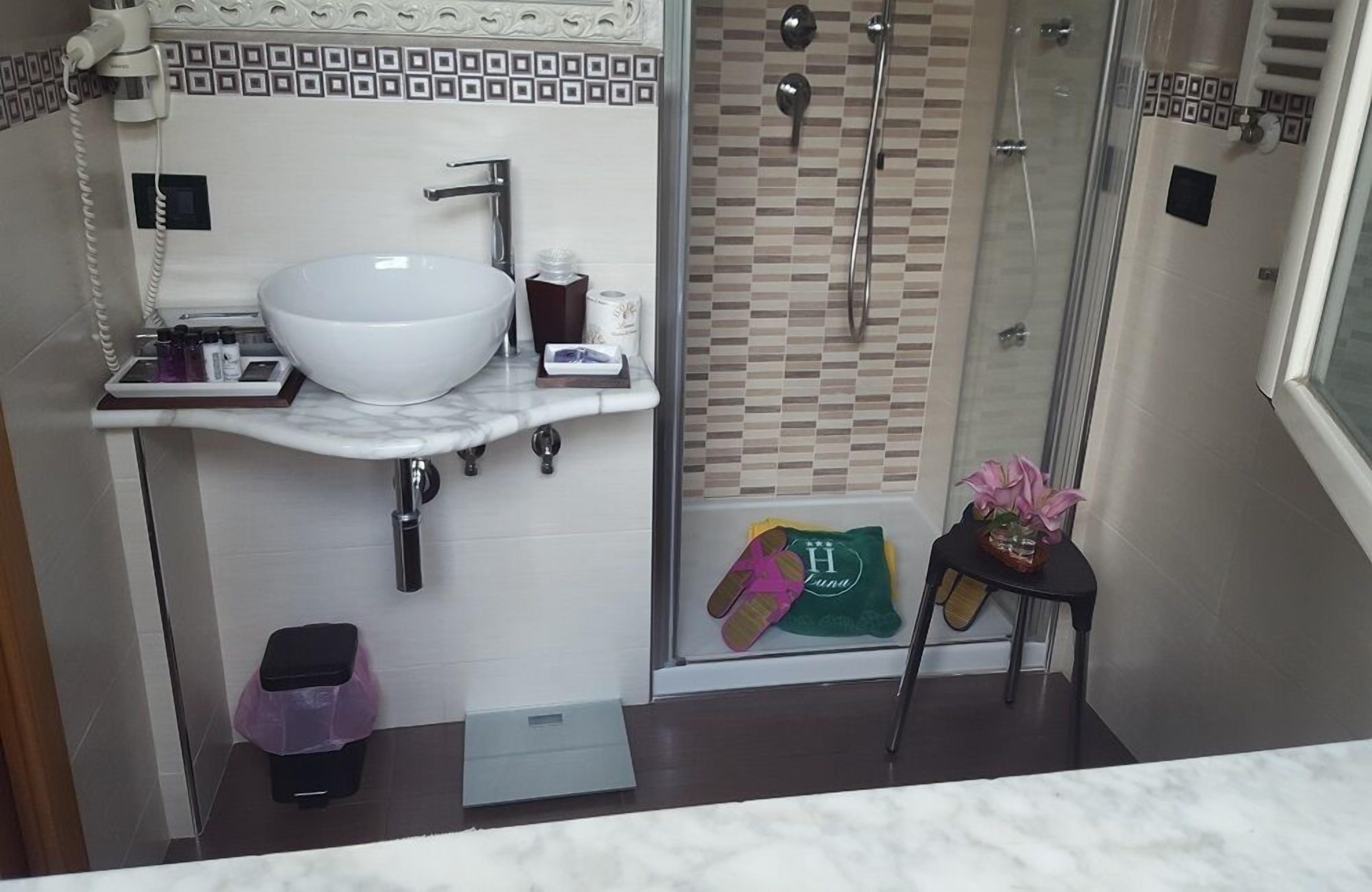 A bathroom with a white sink, a glass shower enclosure, and a small table with a vase of flowers.