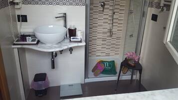 Une salle de bain avec un lavabo blanc, une cabine de douche en verre et une petite table sur laquelle est posé un vase de fleurs.
