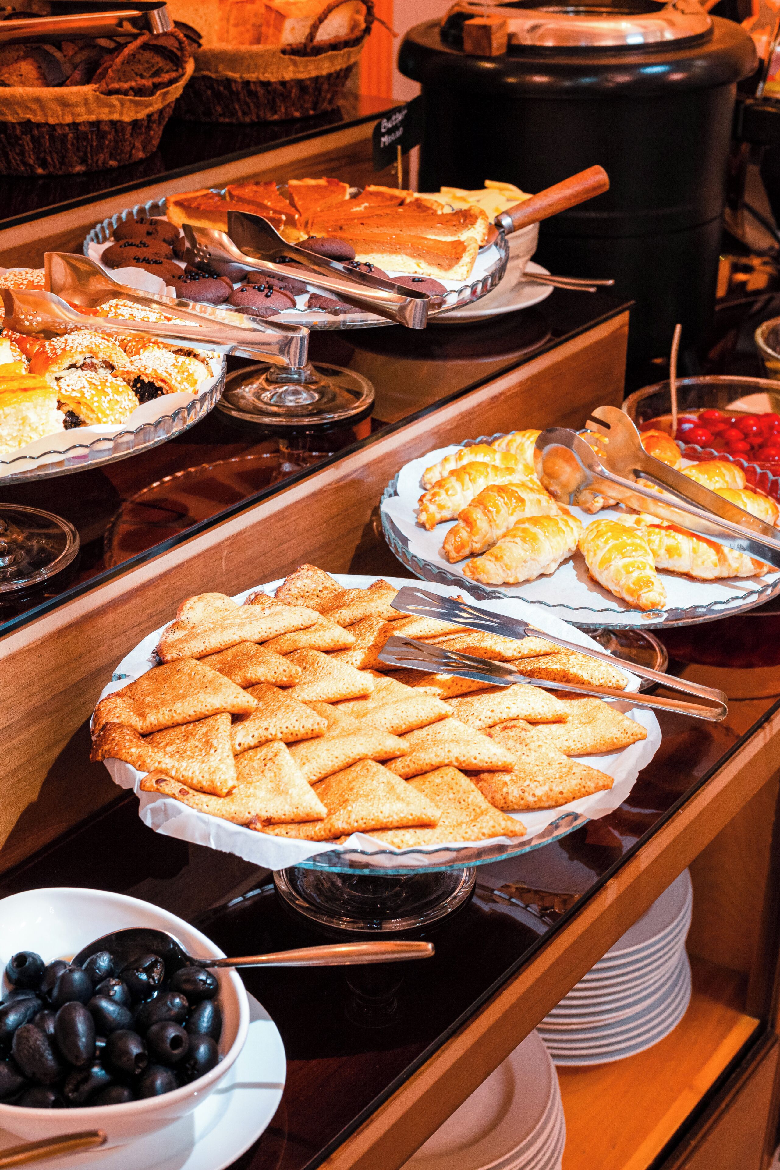 A buffet with various food items including pies, pastries, and a bowl of olives.