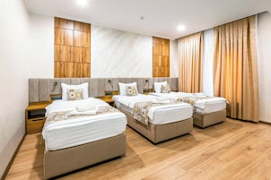 Habitación de hotel con tres camas, paredes de paneles de madera y un ventanal con cortinas.