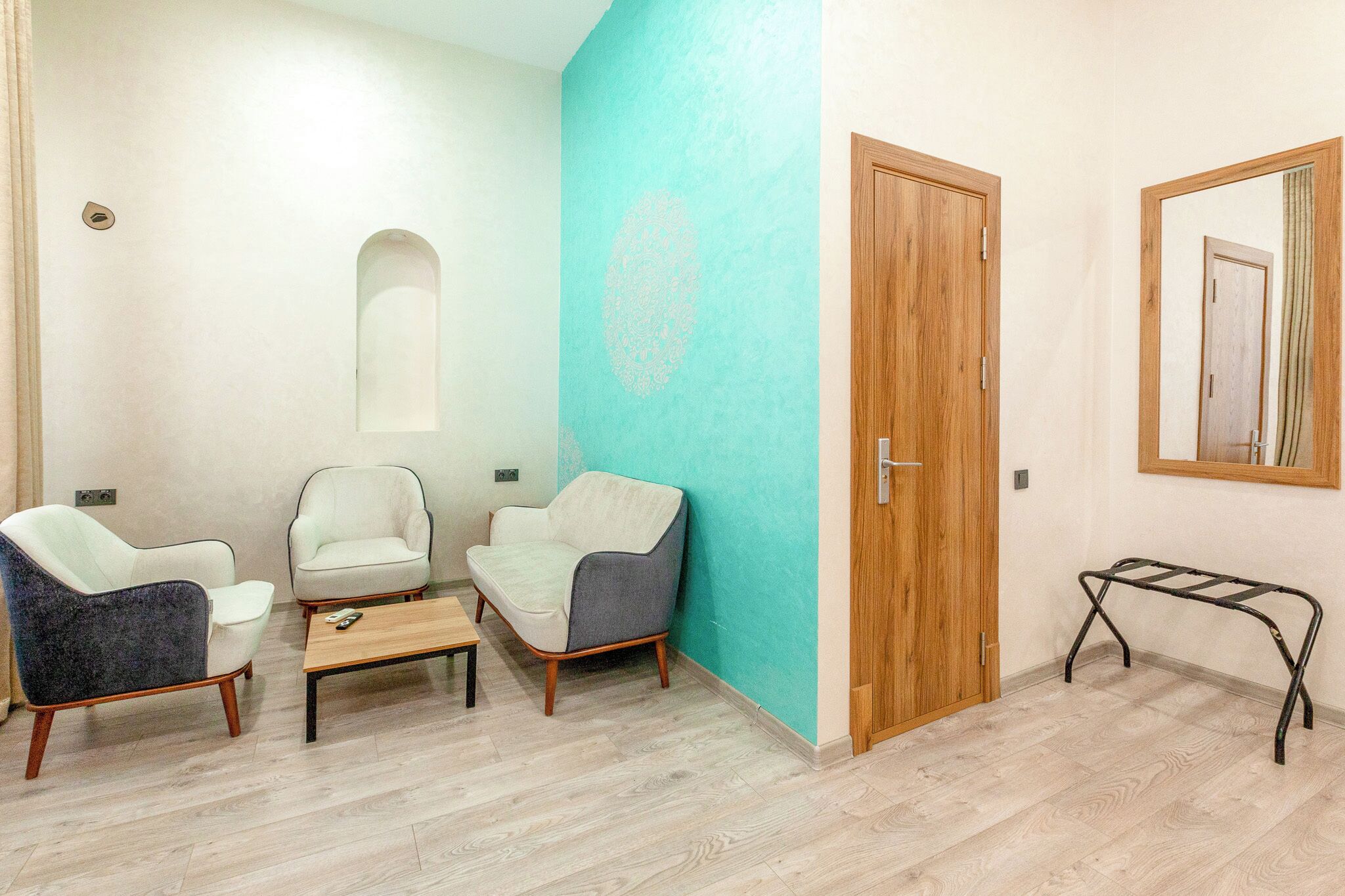 A room with three chairs, a small table, a wooden door, and a mirror on the wall.