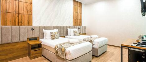 A hotel room with two beds, a wooden headboard, a small table, and a trash bin.