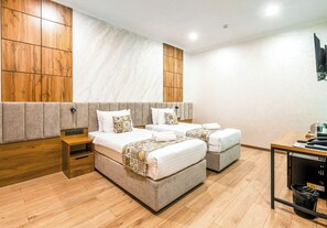 A hotel room with two beds, a wooden headboard, a small table, and a trash bin. - Khan Hotel Bukhara (Bukhara)