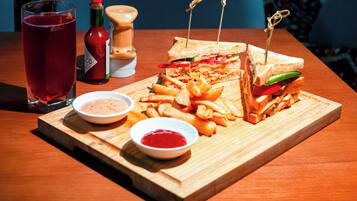 A wooden table with a sandwich cut in half, a plate of fries, a glass of red drink, and two small bowls of condiments.