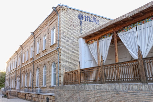 Il s’agit d’un bâtiment historique sur lequel on peut lire l’inscription « Hôtel Malika ». Il se distingue par sa façade en briques, ses grandes fenêtres et un balcon en bois agrémenté de rideaux.