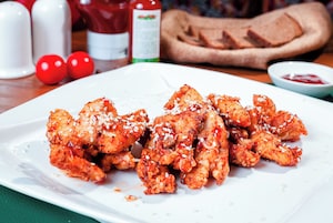 Un plato de pollo con semillas de sésamo y una guarnición de kétchup.