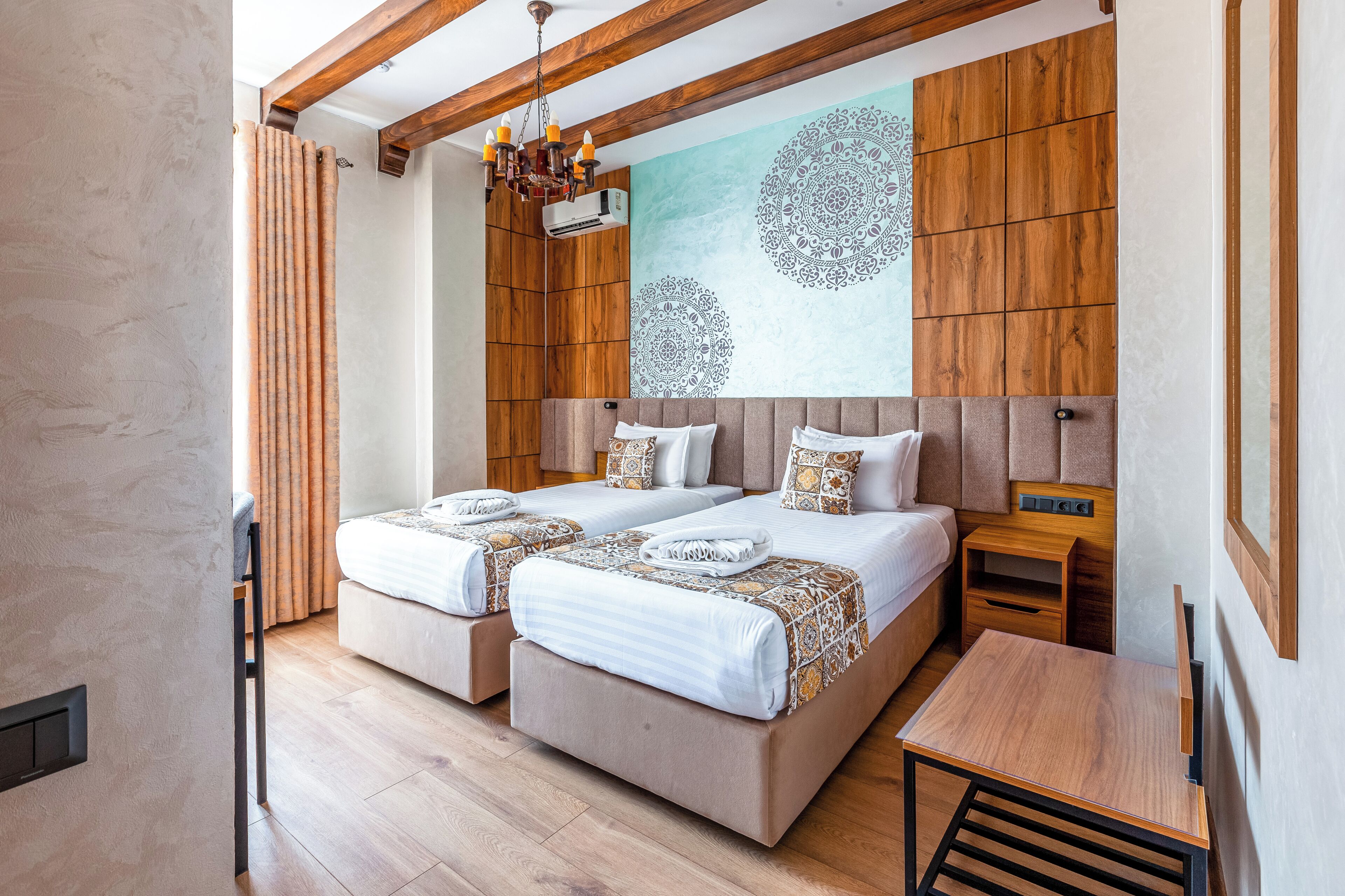 A hotel room with two beds, a wooden headboard, a wall mural, and a small wooden table.
