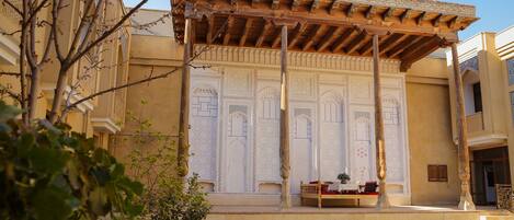 Un patio con una zona de estar techada, un muro decorativo con diseños intrincados y un suelo de ladrillo.