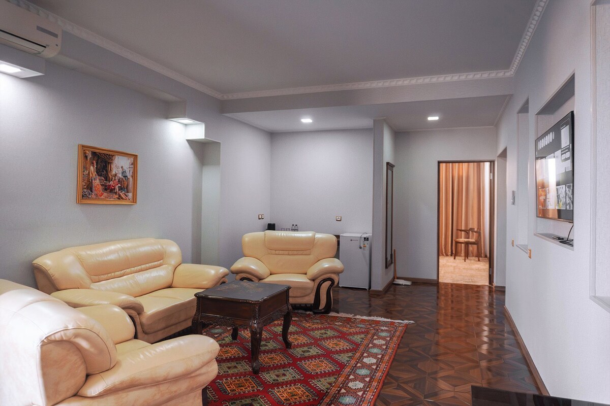 A living room with a sofa, armchair, and a patterned rug.