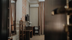 Una habitación con escritorio, silla y televisor. Hay un radiador y cortinas en las ventanas.