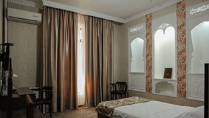Una habitación de hotel con cama, escritorio, dos sillas y ventana con cortinas.