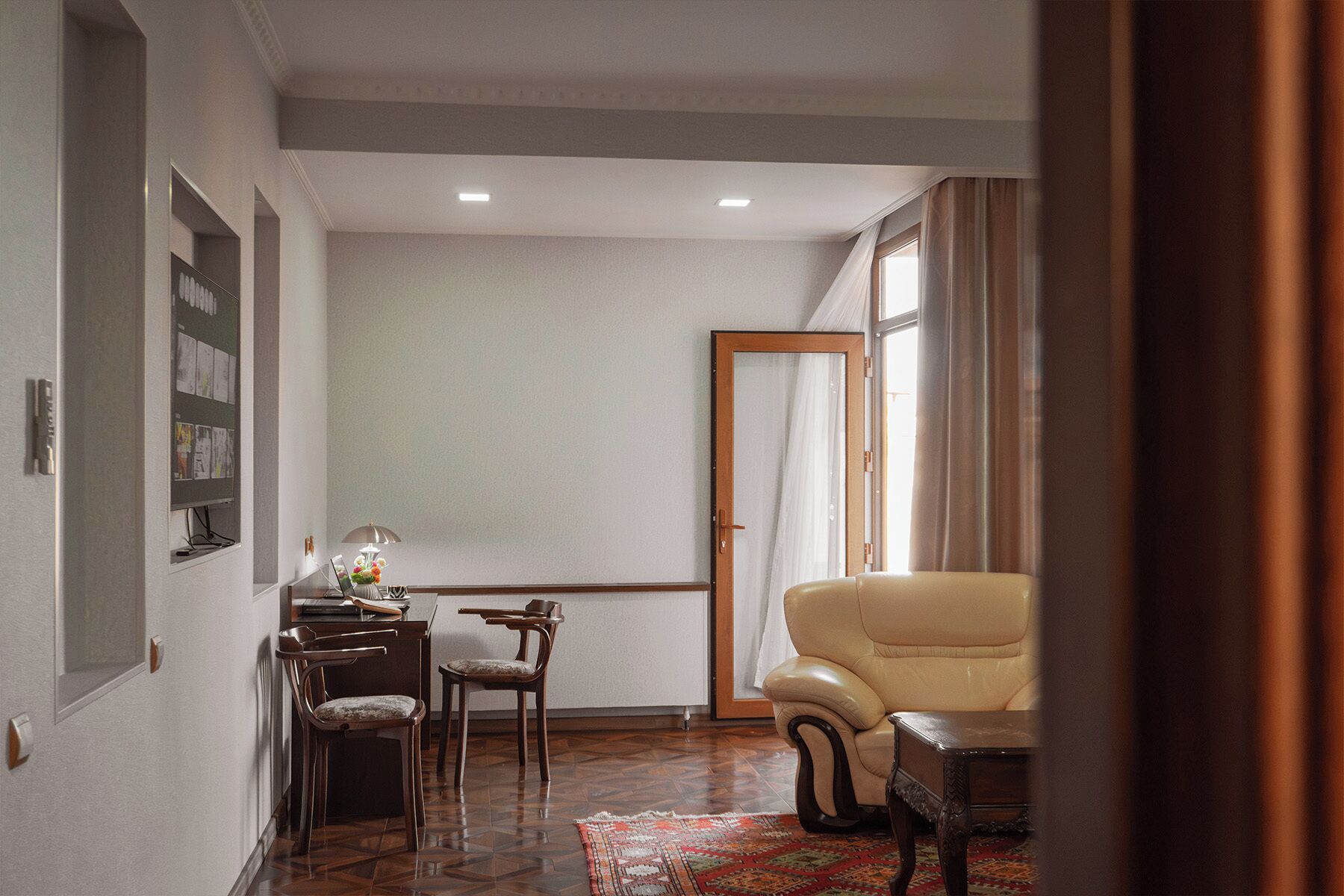 A room with a dining table, chairs, a sofa, a patterned rug, and a door leading to another room.