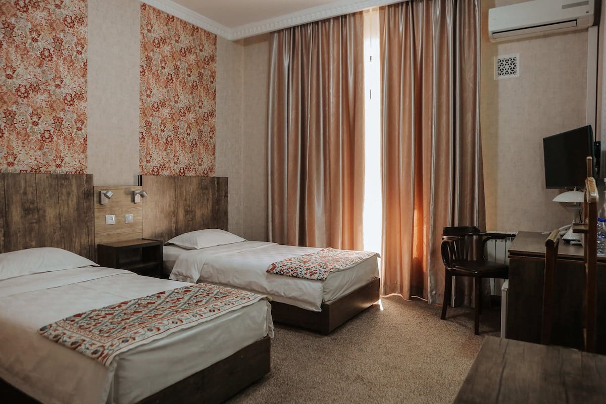 A hotel room with two beds, a desk, a chair, and an air conditioning unit.