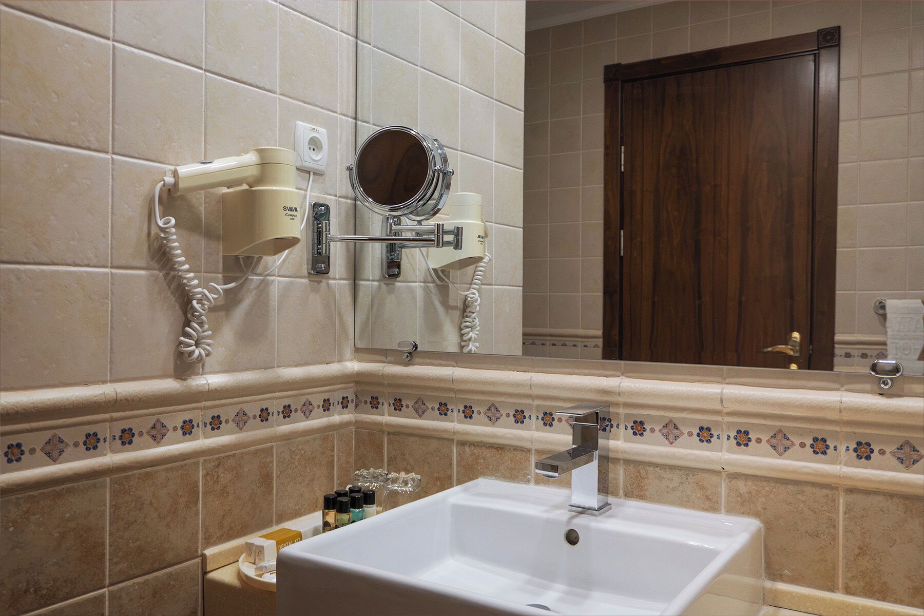 A bathroom with a white sink, a mirror, and a hairdryer mounted on the wall.