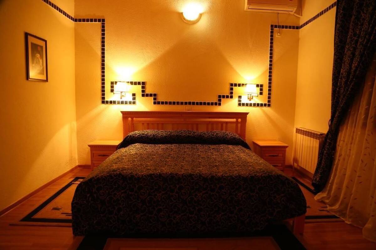 Habitación de hotel con cama, mesitas de noche, un espejo y una lámpara fijada a la pared.