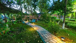 A paved pathway in a lush garden area with benches and potted plants. - Asia Bukhara Hotel (Bukhara)