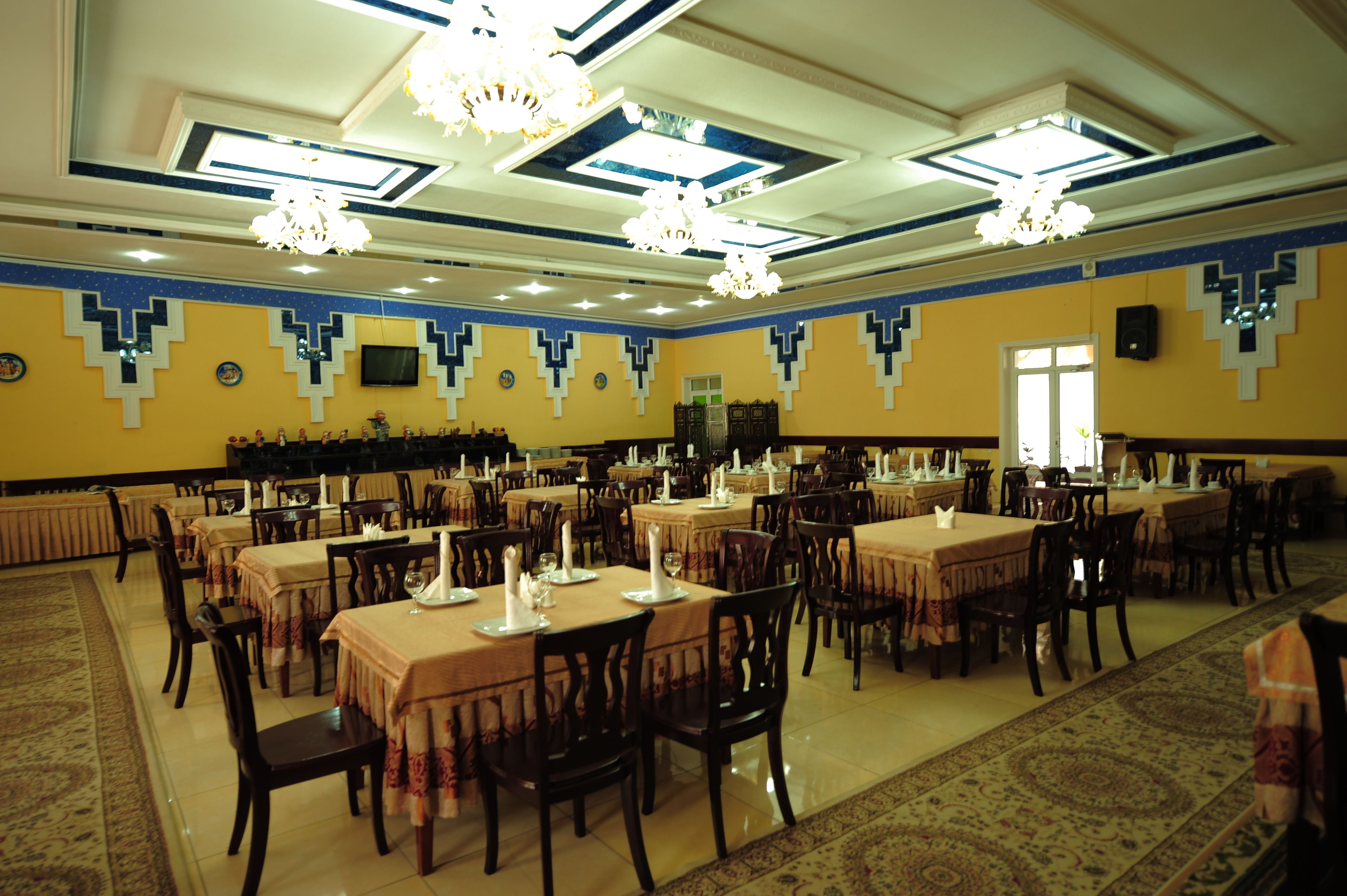 Une grande salle à manger avec de nombreuses tables et chaises, des lustres et des décorations murales à motifs.