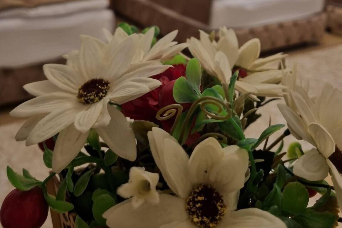 Habitació d'hotel amb dos llits, cadascun amb un capçal de fusta i roba de llit blanca. Hi ha una nit de nit entre els llits amb una làmpada. Un ram de flors artificials al primer pla.