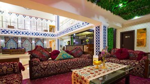 A spacious lobby with a high ceiling, patterned walls, and a central seating area with a table and cushions. - Asia Bukhara Hotel (Bukhara)