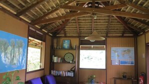 A room with a wooden ceiling, a map on the wall, a bookshelf, a table with a purple tablecloth, and a chair. - Vaianae Lodge (Moorea-Maiao)