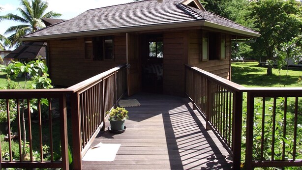 A wooden house with a covered porch and a small garden. - Vaianae Lodge (Moorea-Maiao)