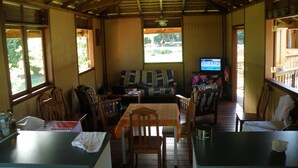 A cozy room with a wooden ceiling, a television, a table with chairs, and a window with a view of greenery. - Vaianae Lodge (Moorea-Maiao)