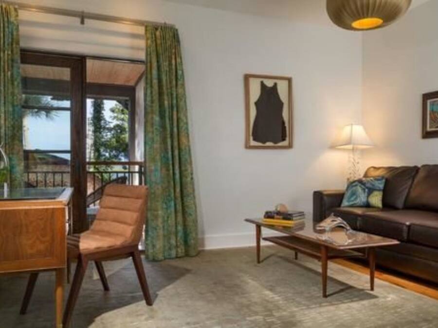 A living room with a brown leather sofa, a wooden coffee table, a brown leather chair, a glass table, and a window with green curtains.