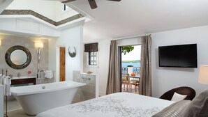 A hotel room with a large bed, a bathtub, a balcony with a view of the sea, and a TV mounted on the wall. - Black Dolphin Inn (New Smyrna Beach)