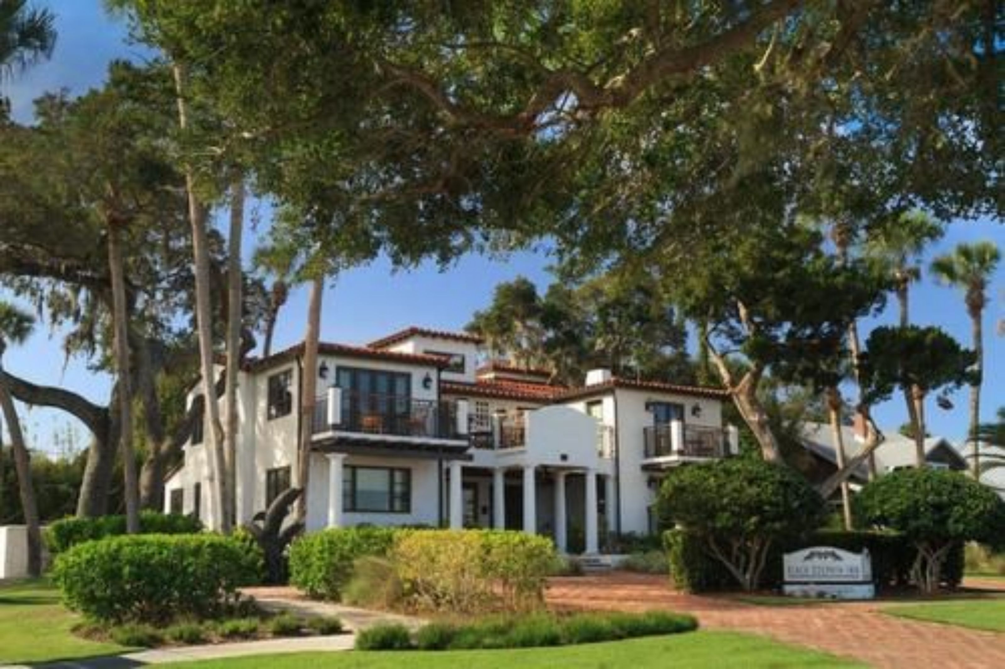 A two-story house with a white exterior, surrounded by mature trees and a well-maintained lawn.