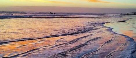 A beach with waves and a sunset.