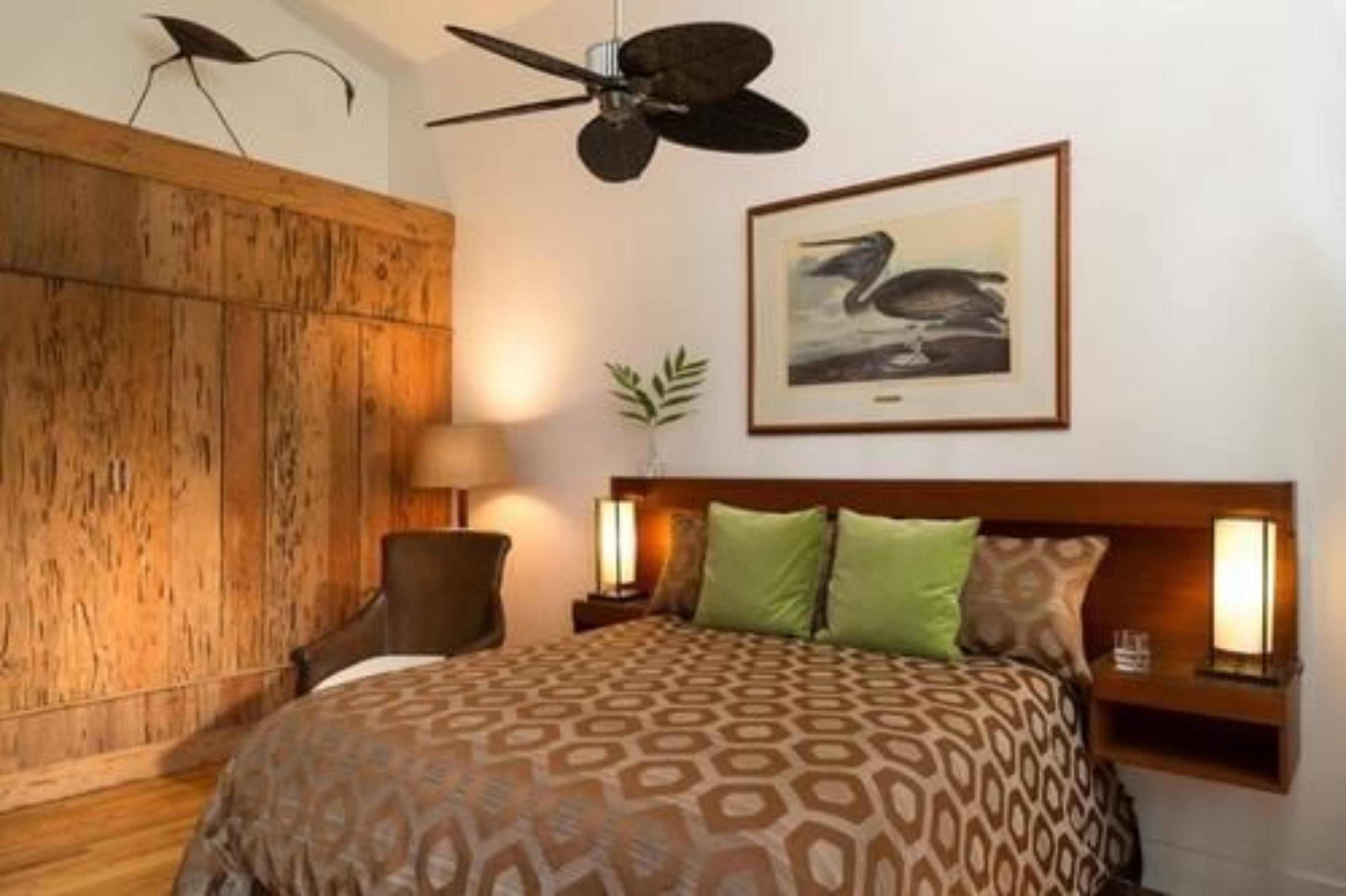 A bedroom with a patterned bedspread, a ceiling fan, a framed picture on the wall, and bedside lamps.