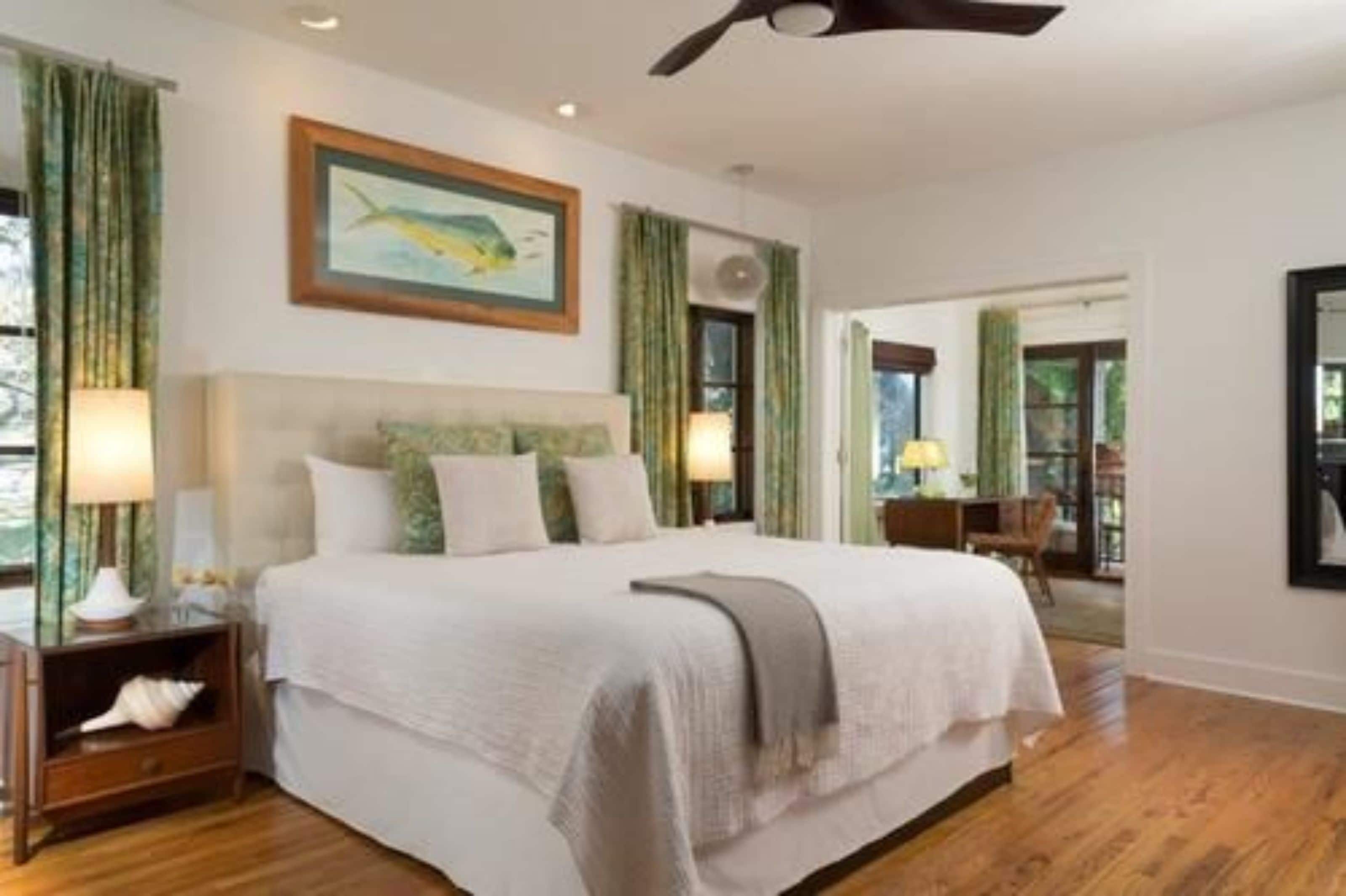 A bedroom with a bed, nightstands, a ceiling fan, and a painting on the wall.