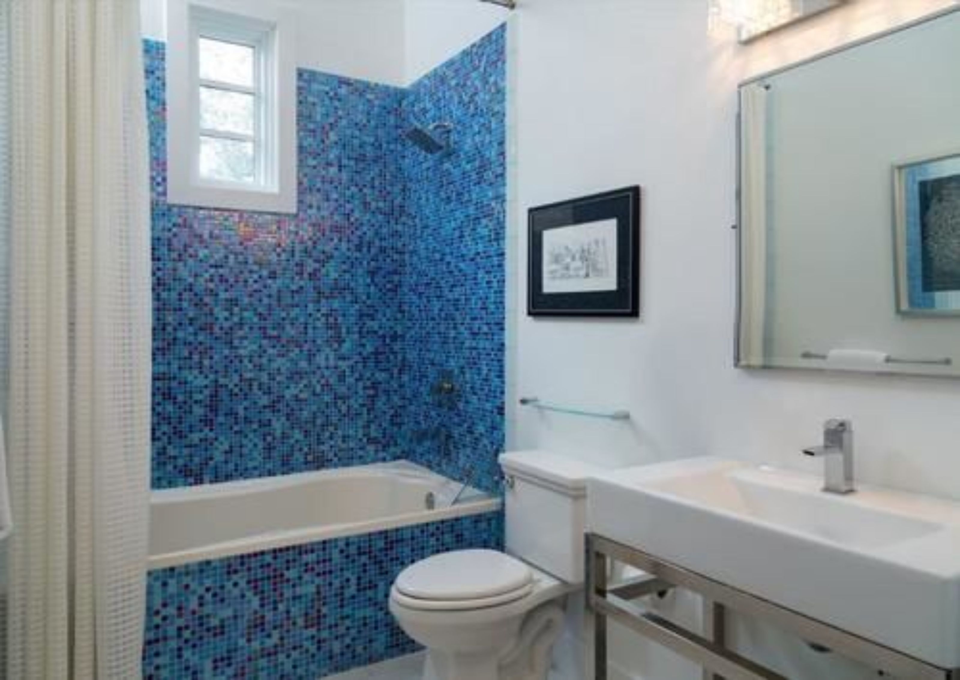A bathroom with a mosaic tile shower wall, a framed picture on the wall, and a white sink.