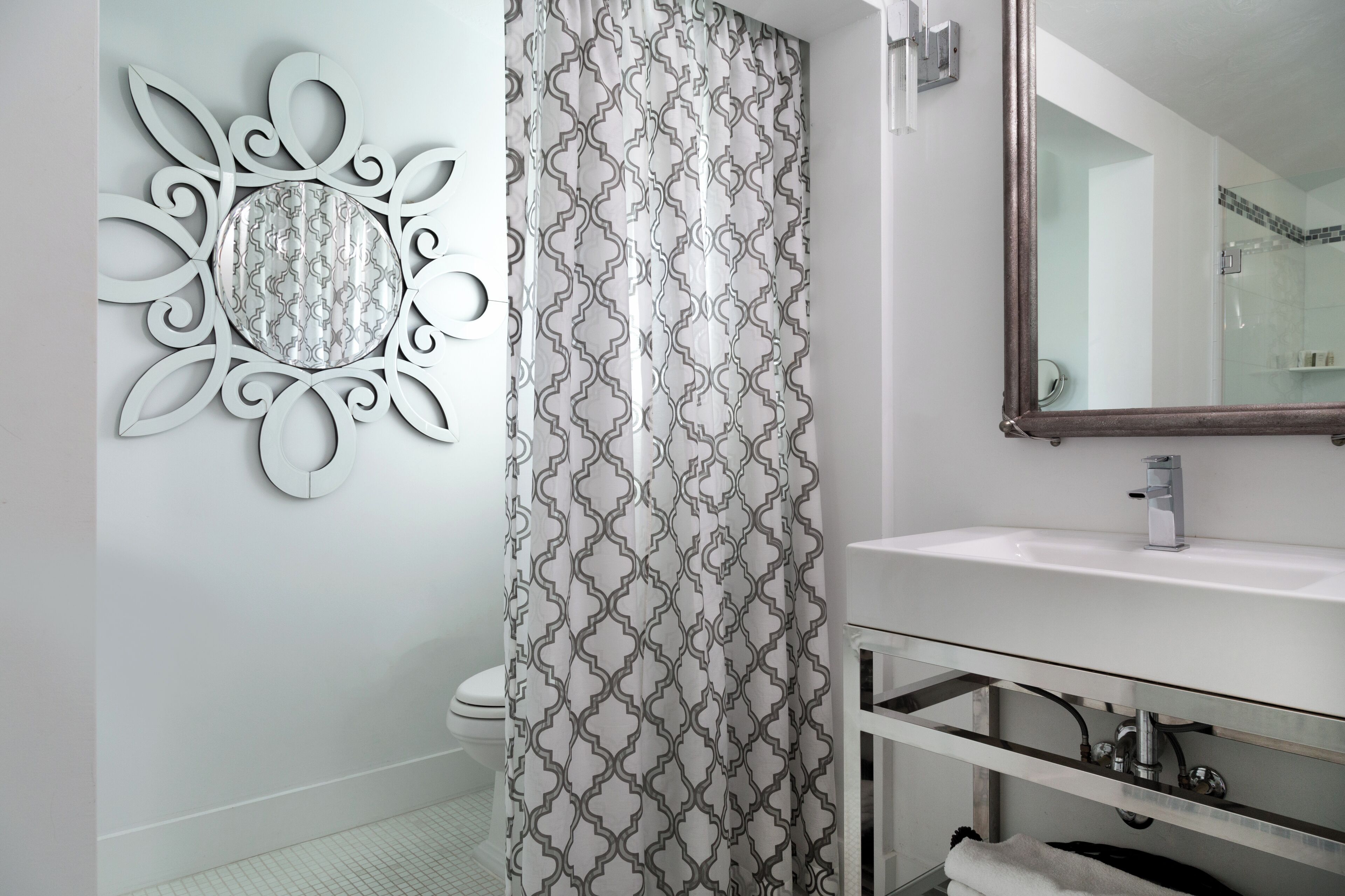 Un baño con un lavabo blanco, un espejo y una cortina de ducha con diseño geométrico.