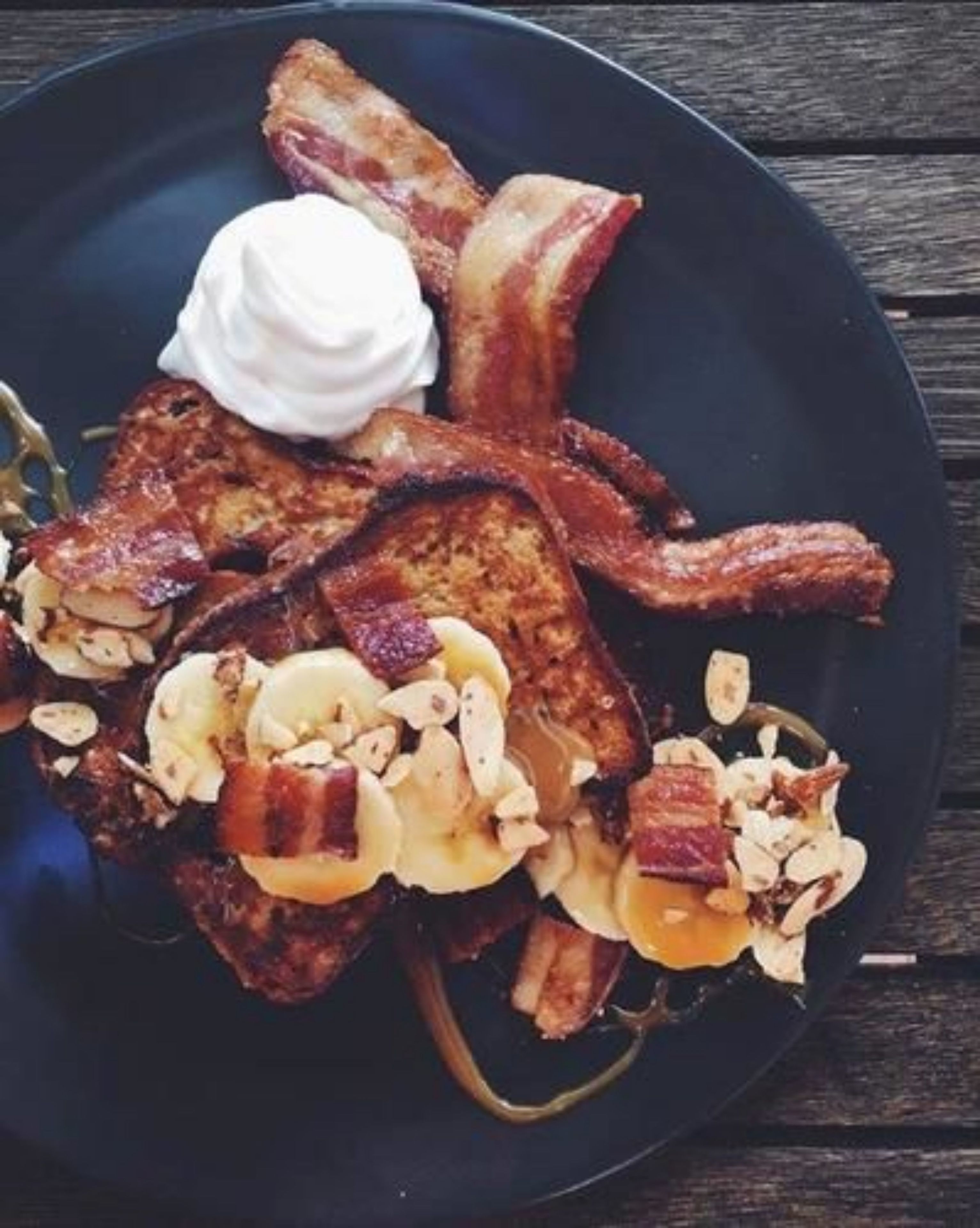 A plate of French toast with bananas, nuts, and a dollop of whipped cream.