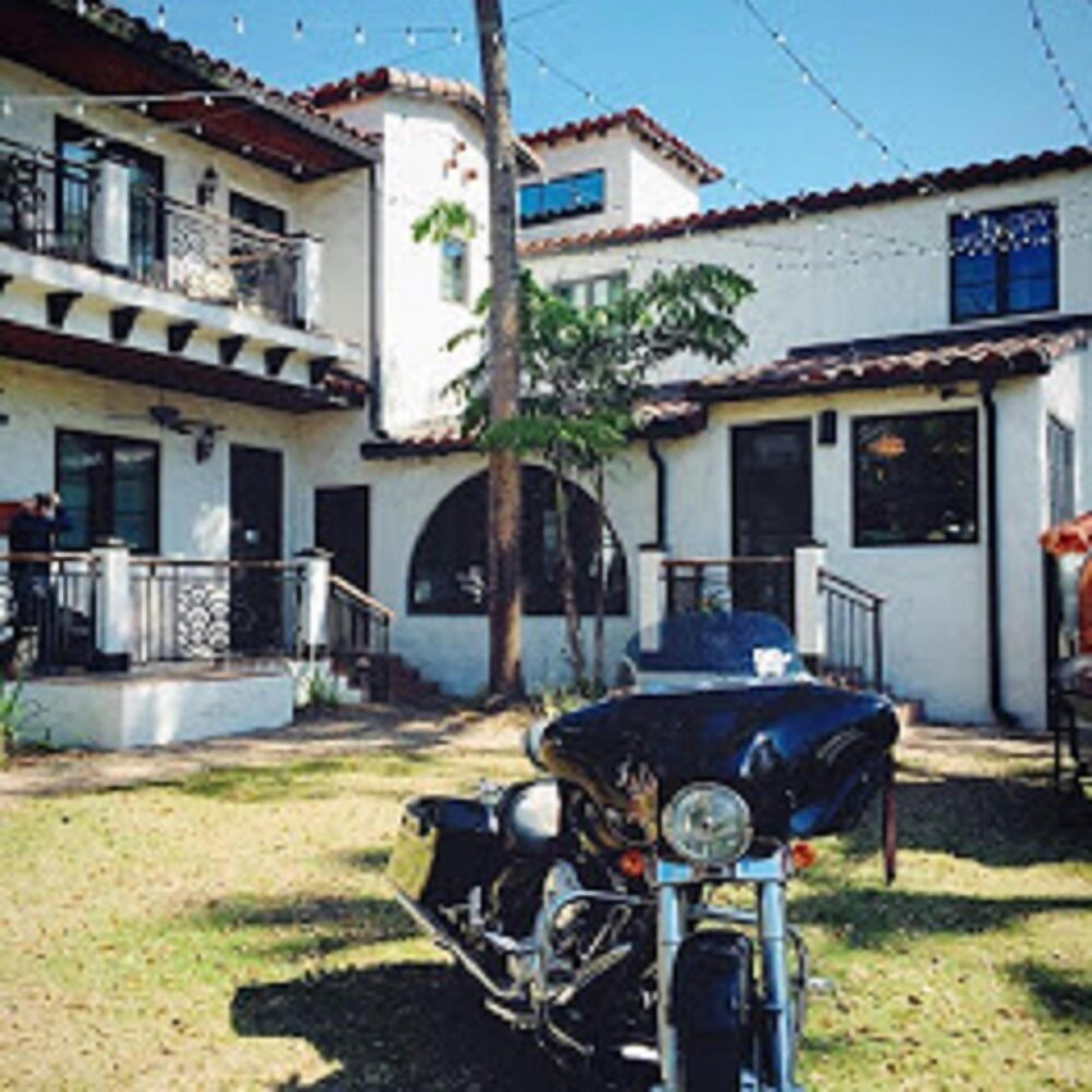 A two-story building with a balcony, a motorcycle parked in front, and a clear sky.