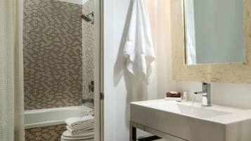 A bathroom with a tiled shower, a white sink, and a mirror.