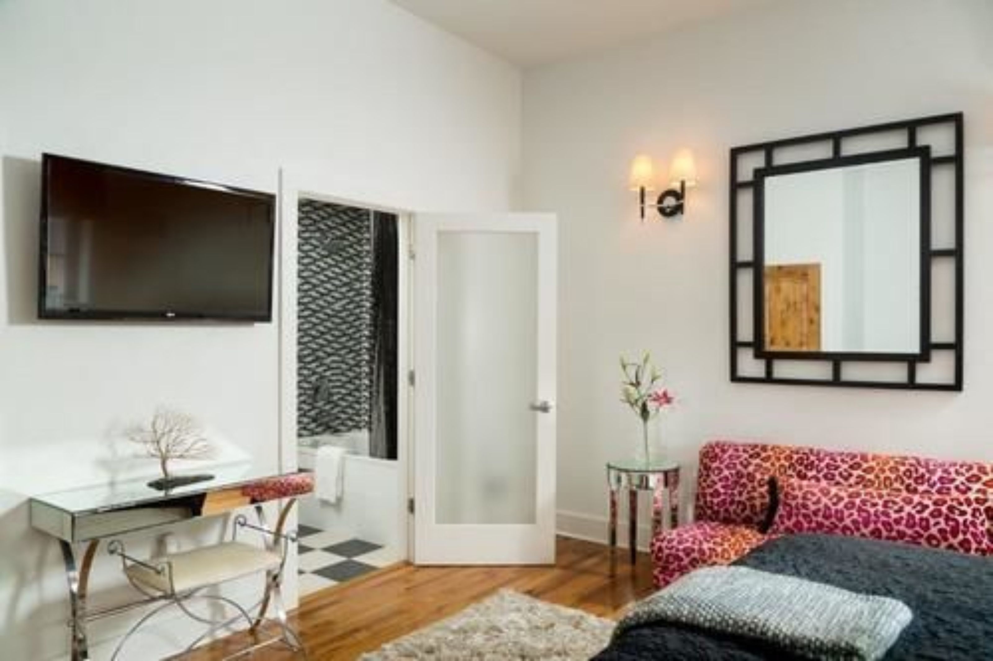 A bedroom with a bed, a desk, a chair, a TV, a mirror, and a door.