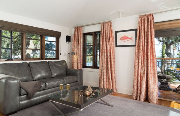 A modern living room with a leather sofa, a glass coffee table, and a view of the outdoors through large windows.