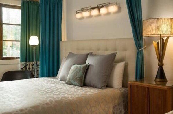 A hotel room with a large bed, a nightstand, a lamp, and a window with curtains. - Black Dolphin Inn (New Smyrna Beach)