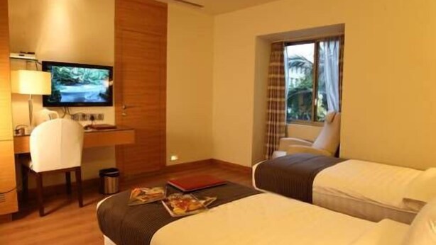 A hotel room with two beds, a desk with a chair, a television, and a window with curtains. - Middleton Inn (Kolkata)