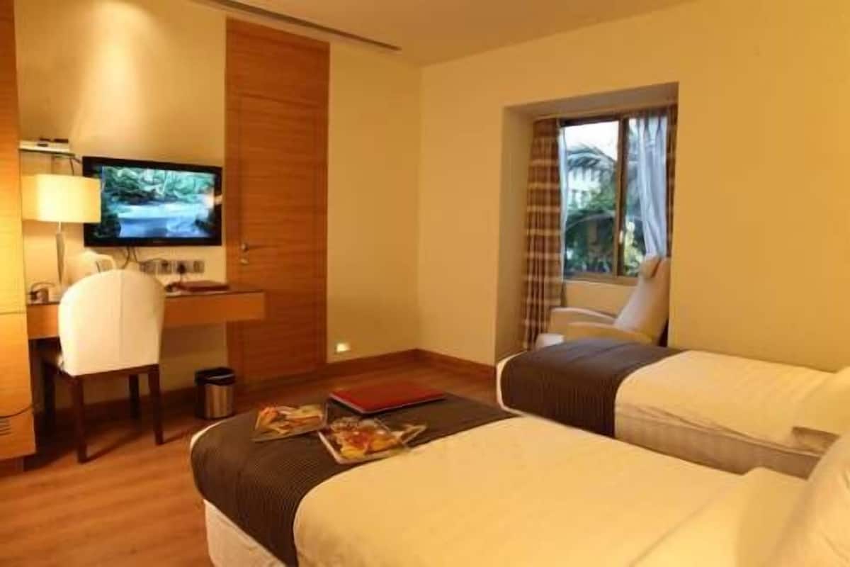 A hotel room with two beds, a desk with a chair, a television, and a window with curtains.