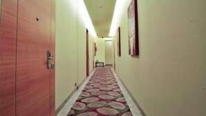 A hotel hallway with wooden doors, a patterned carpet, and framed pictures on the walls. - Middleton Inn (Kolkata)