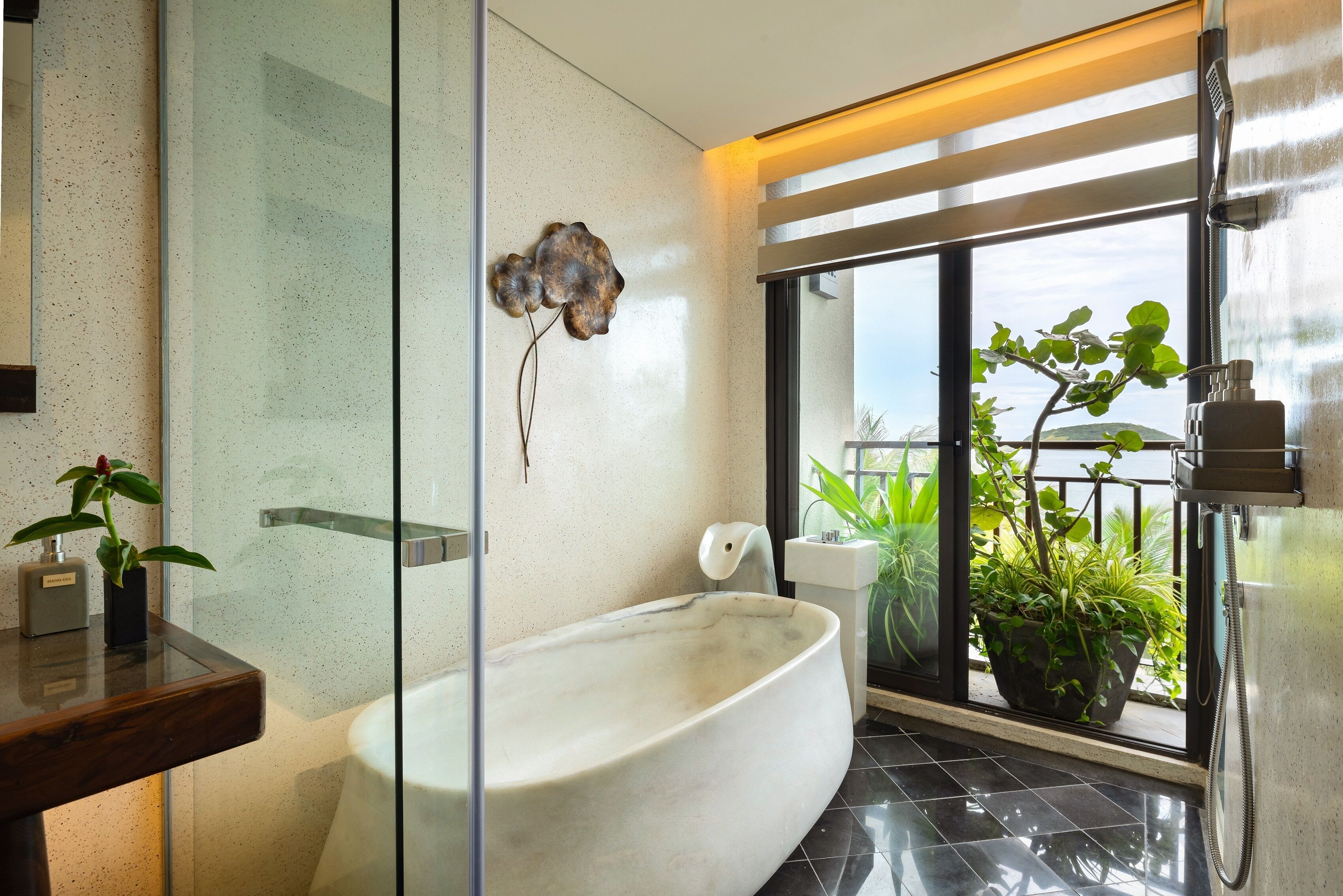 A modern bathroom with a freestanding bathtub, a glass shower enclosure, and a balcony with potted plants.