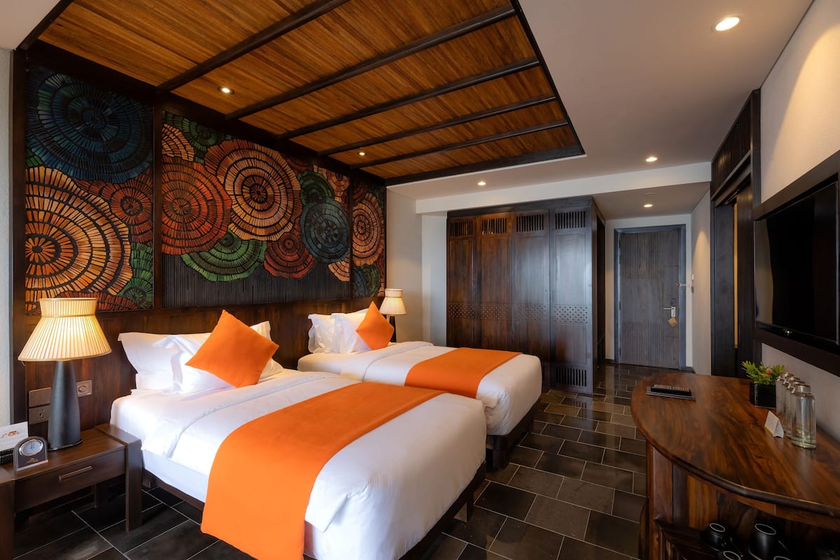 Une chambre d’hôtel avec deux lits, un plafond en bois, une fresque murale, un téléviseur et une table de chevet en bois.