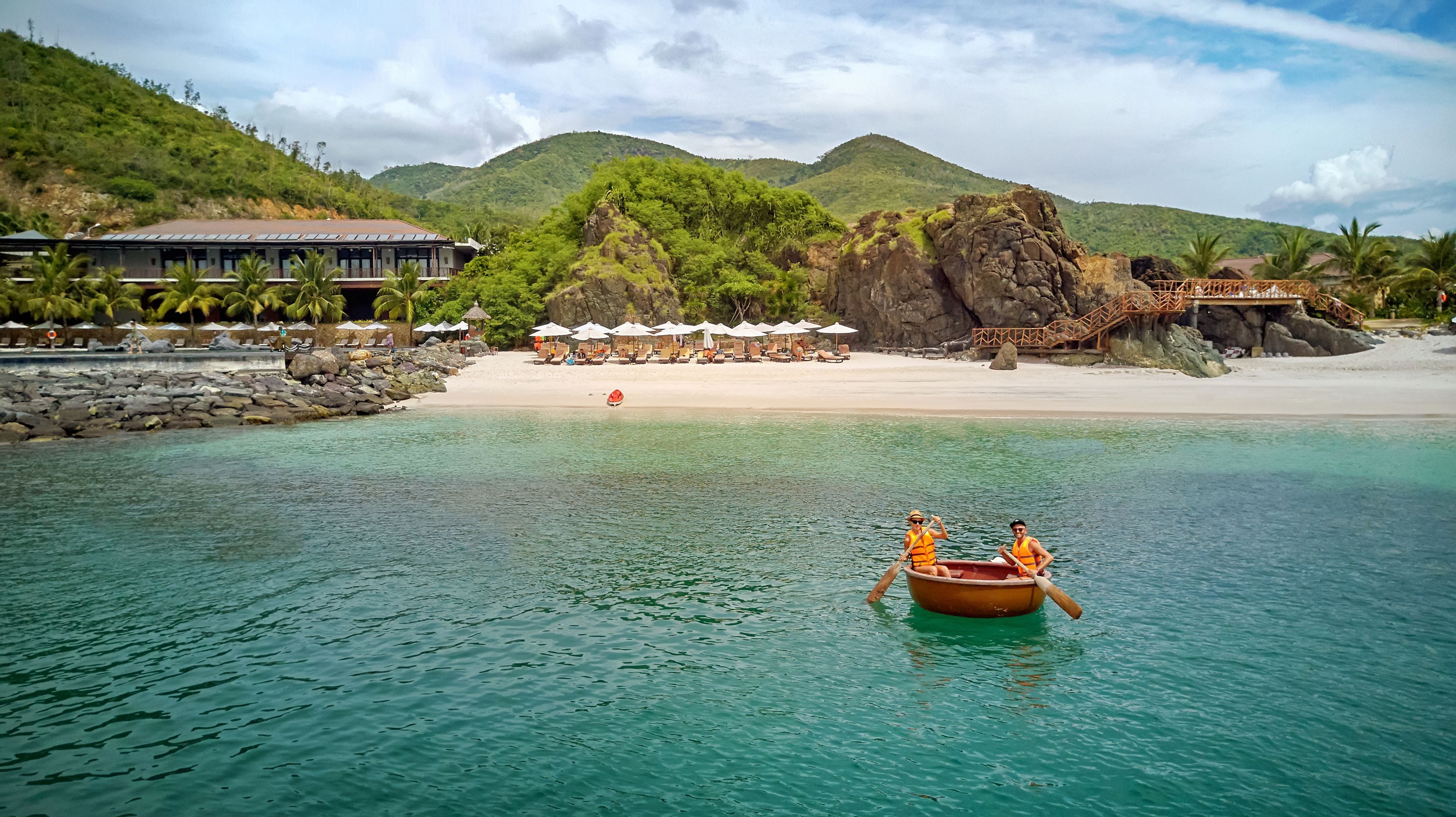 A beach resort with a clear view of the ocean, a rocky outcrop, and a lounge area with umbrellas.