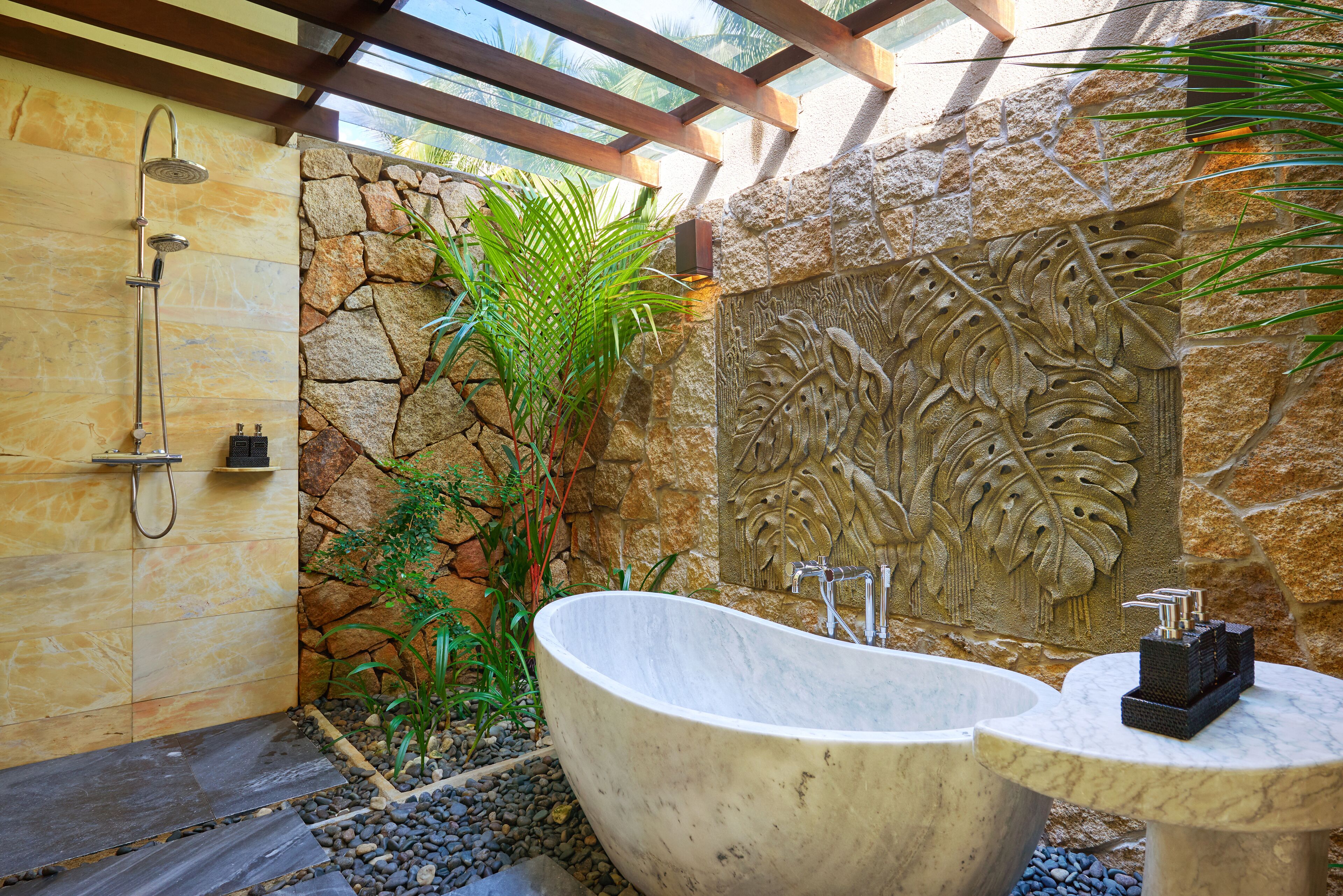 Un baño con una bañera independiente, ducha y pared de piedra con diseño de hojas.