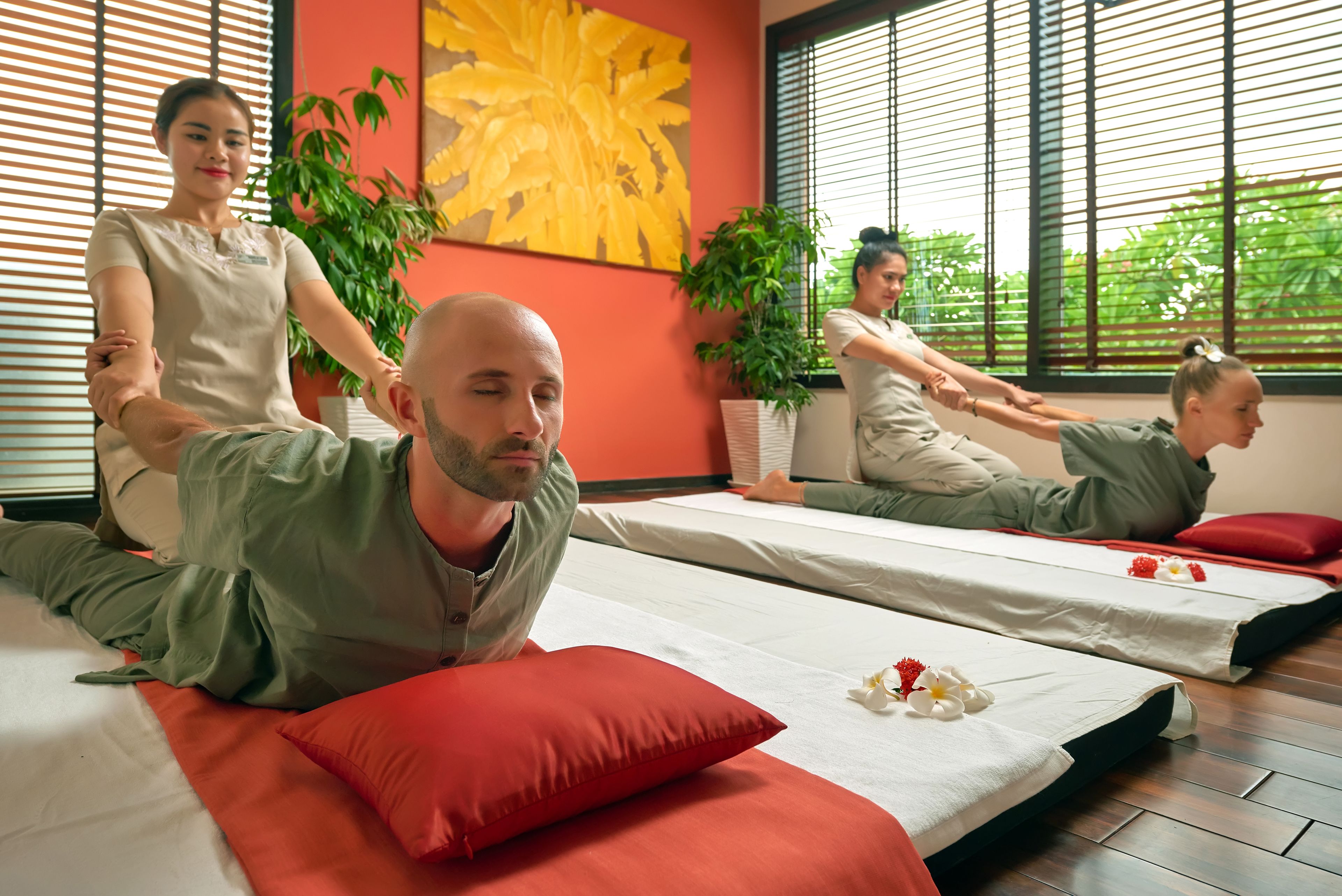 Une salle de massage équipée de deux tables de massage, de coussins rouges et d’un grand tableau représentant des fleurs jaunes accroché au mur.