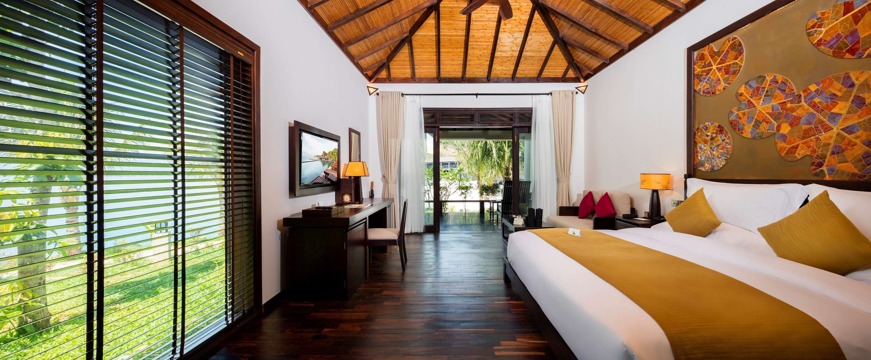 Habitación de hotel con cama, escritorio, silla, televisor y vistas al exterior.
